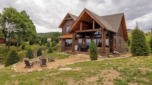 Une grande cabane rustique en rondins de bois, dotée d’une vaste terrasse et d’un espace salon extérieur.