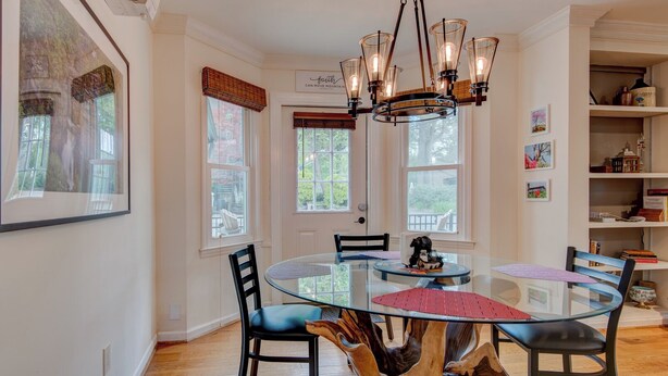 A dining area with a glass table surrounded by chairs, a wooden tree stump centerpiece, and a chandelier. - The Wander Inn (Blowing Rock)