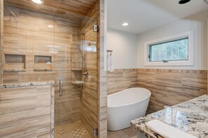 Un baño moderno con ducha de vidrio, bañera independiente y encimera de mármol.