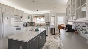 A modern kitchen with white cabinetry, a central island, and a dining area with a table and chairs. - Hilltop Hideaway (Boone)