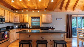 Une cuisine avec des meubles en bois, un îlot central doté de tabourets et une vue sur l’extérieur par une fenêtre.