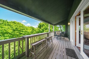 A covered outdoor deck with wooden benches and a table, overlooking a lush green landscape. - Antlers Lodge (Blowing Rock)