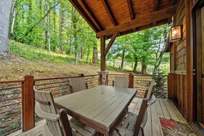 Une terrasse en bois, agrémentée d’une table et de chaises, entourée d’une balustrade en bois, et offrant une vue sur une zone boisée.