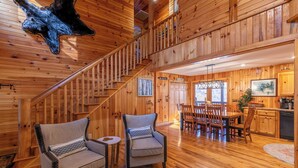 A spacious log cabin interior with a central staircase, a dining area, and a kitchen. - Riverbend Retreat (Todd)