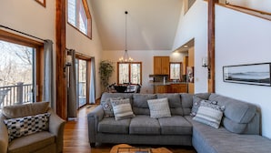 A spacious living room with a grey sectional sofa, a small armchair, and a coffee table. A dining area with a table and chairs is visible in the background. - A Change of Scenery at Yonahlossee (Boone)