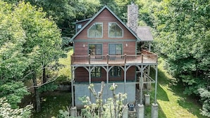 A two-story wooden cabin with a balcony, surrounded by dense forest. - A Change of Scenery at Yonahlossee (Boone)