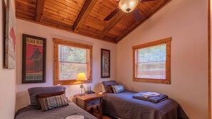 A cozy room with two beds, wooden ceiling beams, and large windows with blinds. - Knotty Pine (West Jefferson)