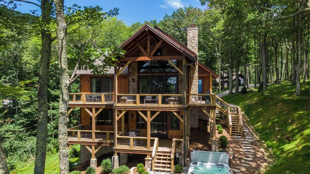 A wooden cabin with a stone chimney, a hot tub, and a deck with outdoor seating. - Blue Ridge View at Eagles Nest (Banner Elk)