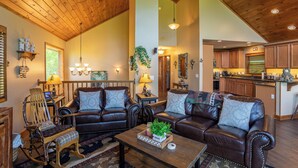 A spacious living room with a high ceiling, leather sofas, a wooden rocking chair, and a kitchen in the background. - Bearadise Cabin (Banner Elk)