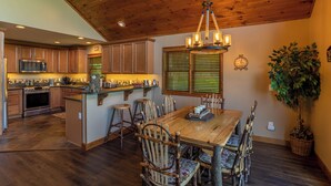 A kitchen with wooden cabinets, a central island, bar stools, and a dining table. - Bearadise Cabin (Banner Elk)