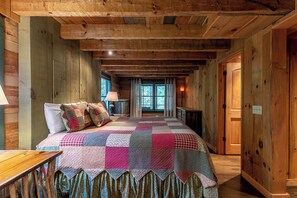 Camera da letto in una baita di legno, con un letto grande, un comodino, una finestra e una porta.
