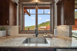 A kitchen with a large window, granite countertop, stainless steel sink, and wooden cabinets. - Cloud Catcher at Eagles Nest (Banner Elk)