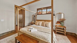 Una cama con dosel de madera, una mesita de noche, un espejo y una ventana con vistas a edificios.