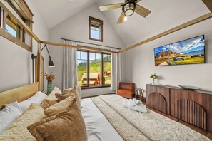 A bedroom with a large bed, a ceiling fan, a window with curtains, a painting, and a wooden cabinet. - Cloud Catcher at Eagles Nest (Banner Elk)