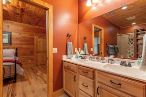A wooden cabin-style bathroom with a large mirror, wooden cabinets, and a white sink. - The Forge (Lansing)