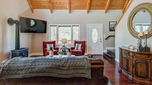 Une pièce chaleureuse avec un plafond en bois, une cheminée, une télévision, un grand miroir et un coin salon confortable avec un canapé et des fauteuils.