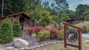 A wooden cabin with a deck, surrounded by trees and shrubs. - Hook Wine and Sinker at Eagles Nest (Banner Elk)
