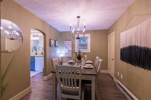 A dining area with a wooden table, white chairs, a chandelier, and a large mirror on the wall. - Hot Toddy Cottage (Boone)