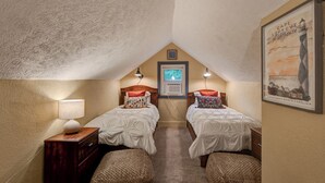 Un dormitorio acogedor en el desván con dos camas individuales, un aparador de madera, una lámpara y un cuadro con un faro.
