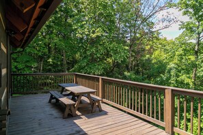 Un patio in legno con tavolo da picnic e panche, circondato da fitta vegetazione.