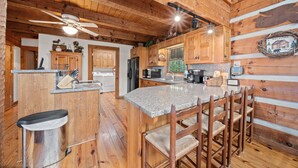 A rustic kitchen with wooden walls, a granite countertop, and a bar area with wooden chairs. - Mountain Masterpeace (Banner Elk)