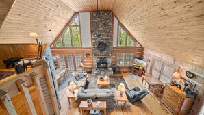 A cozy cabin interior with a stone fireplace, wooden floors, and large windows offering a view of the outdoors. - Mountain Masterpeace (Banner Elk)