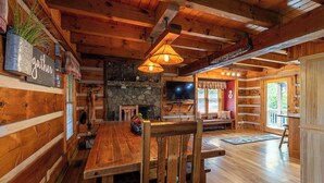A wooden interior with a dining table, chairs, a stone fireplace, and a television. - Cari's Rivers Edge (Boone)