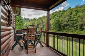 A wooden deck with a table and chairs, overlooking a forested area. - River Roost (Todd)