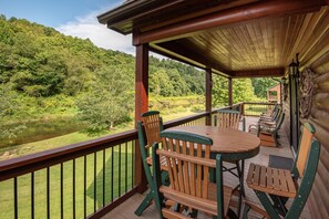 A wooden deck with a table and chairs, overlooking a forested area and a body of water. - River Roost (Todd)