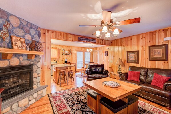 A cabin interior with a stone fireplace, wooden walls, a dining area, and a leather sofa. - River Roost (Todd)