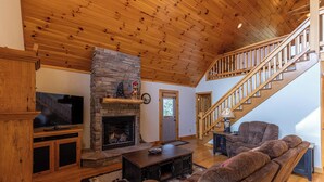 A living room with a stone fireplace, wooden ceiling, and a staircase. - Leafy Way Lodge (Newland)