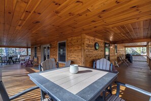 A wooden cabin with a covered deck, a dining table, and several chairs.