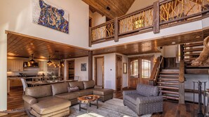 A spacious living area with a large sectional sofa, a patterned armchair, and a wooden coffee table. A staircase with a wooden railing leads to an upper level. - Majestic View Hideaway at Eagles Nest (Banner Elk)
