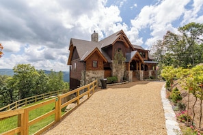 Une cabane rustique en rondins de bois, avec une cheminée en pierre, une allée en gravier et une clôture en bois.