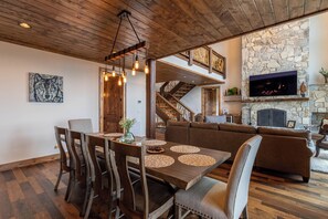 Un espace repas comprenant une table et des chaises en bois, une cheminée en pierre et un escalier menant à un niveau supérieur.