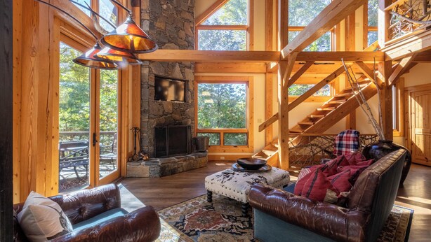 A spacious living room with a stone fireplace, leather sofas, and a wooden staircase. - Cedar Rock Townhomes at Eagles Nest (Banner Elk)