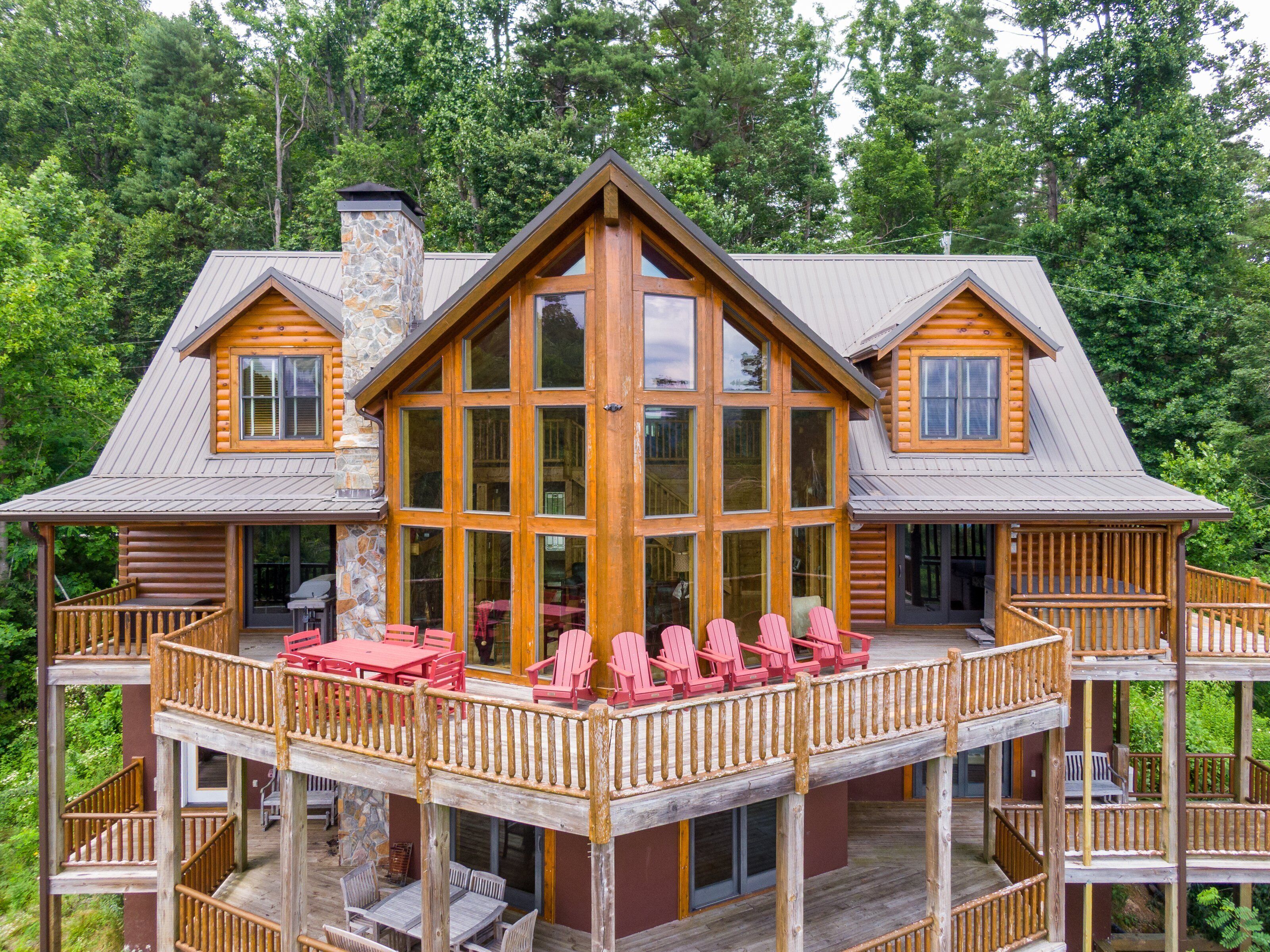 A log cabin with a large deck, multiple windows, and a stone chimney.