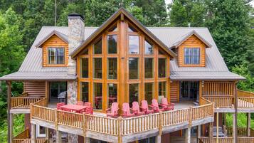 A log cabin with a large deck, multiple windows, and a stone chimney.
