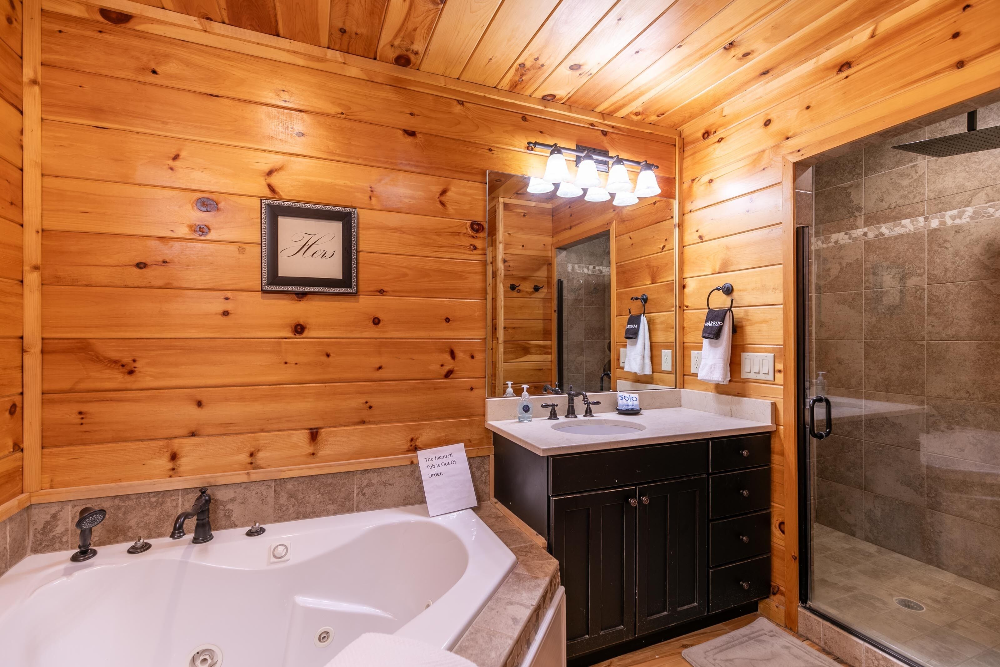 A wooden cabin bathroom with a large bathtub, a shower, and a vanity with a mirror.