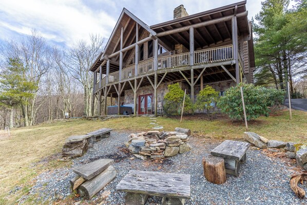A rustic cabin with a stone fireplace, wooden deck, and a stone pathway leading to the entrance. - Highland Mist (Banner Elk)