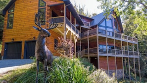 A two-story log cabin with a balcony and a deer sculpture in the foreground. - Rested Traveler (Blowing Rock)