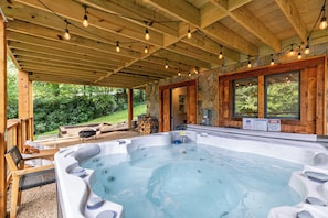 A hot tub area with wooden beams and stone walls, surrounded by outdoor seating and a view of greenery. - Lark Hollow at Linville Land Harbor (Newland)
