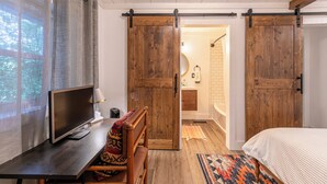 Une chambre à coucher comprenant un lit, un bureau avec une télévision, une chaise et une porte coulissante donnant sur une salle de bain.