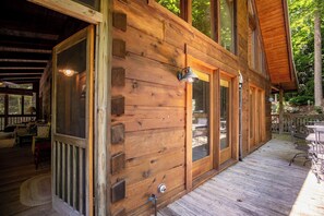 Une cabane en bois dotée d’une véranda, de grandes fenêtres et d’une porte donnant sur un espace intérieur aménagé avec du mobilier.