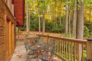 Une terrasse en bois avec une table et des chaises, entourée d’arbres et dotée d’une rambarde en bois.