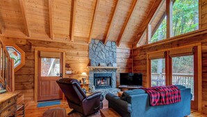 A cozy cabin interior with a stone fireplace, wooden walls, a comfortable sofa, and a television. - Bucks Cabin (Boone)