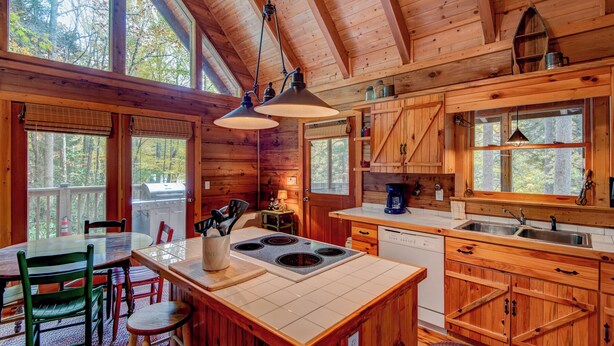 A wooden cabin interior with a dining area, kitchen, and large windows. - Bucks Cabin (Boone)