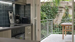 Cocina de diseño moderno, que incluye una estufa, horno y cafetera. Balcón con mesa de madera y vistas a zonas verdes.