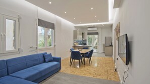 Una sala moderna con un sofá azul, un comedor con mesa y sillas, y una cocina al fondo.
