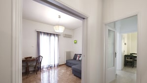 A spacious living area with a wooden herringbone floor, a grey sofa, a dining table with chairs, and a large window with curtains. - Alemar in Kalithea With 1 Bedrooms and 1 Bathrooms (Kallithea)